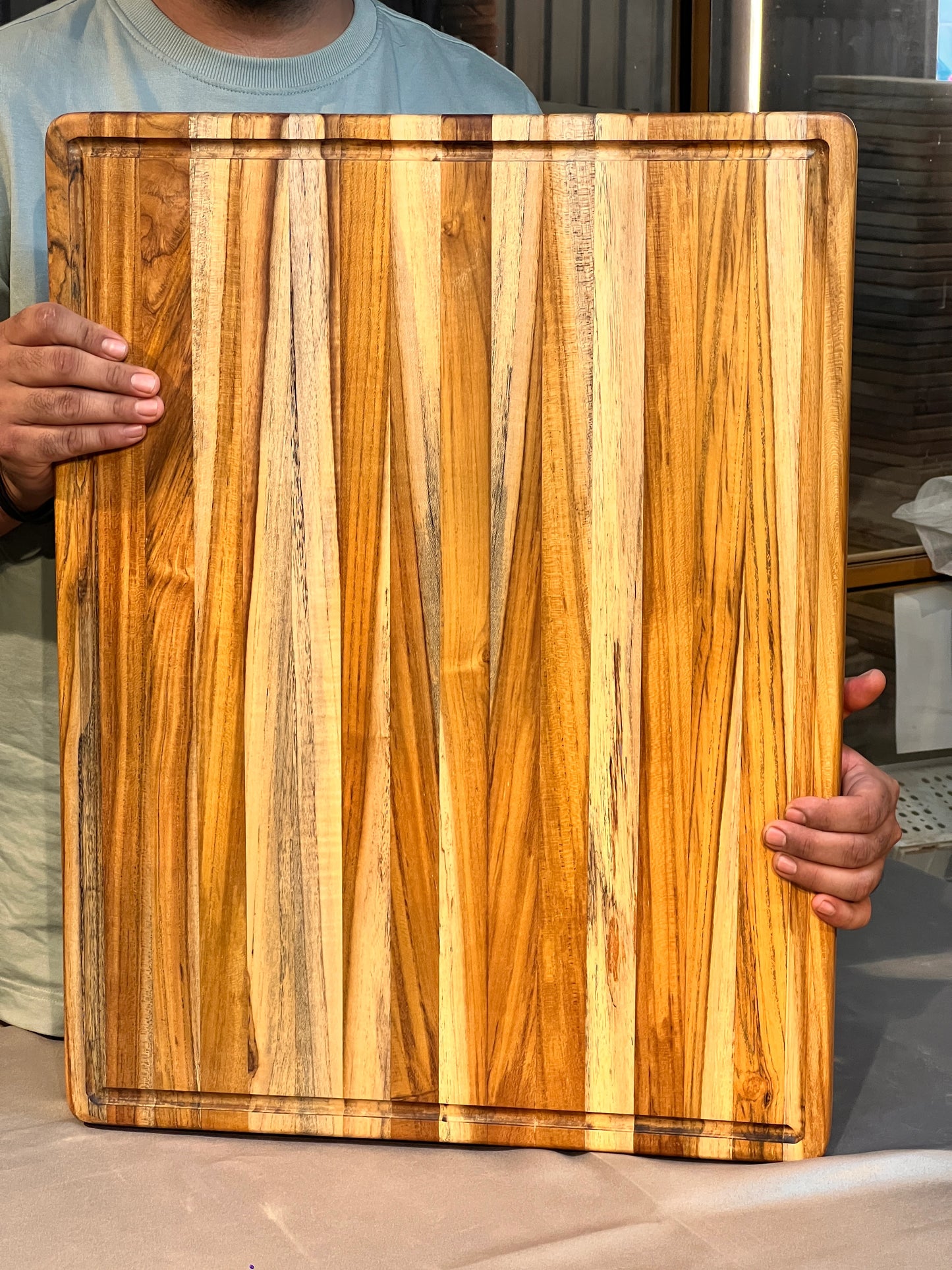 Top view of an edge grain teak wood cutting board measuring 18 x 26 inches, placed on a kitchen countertop.