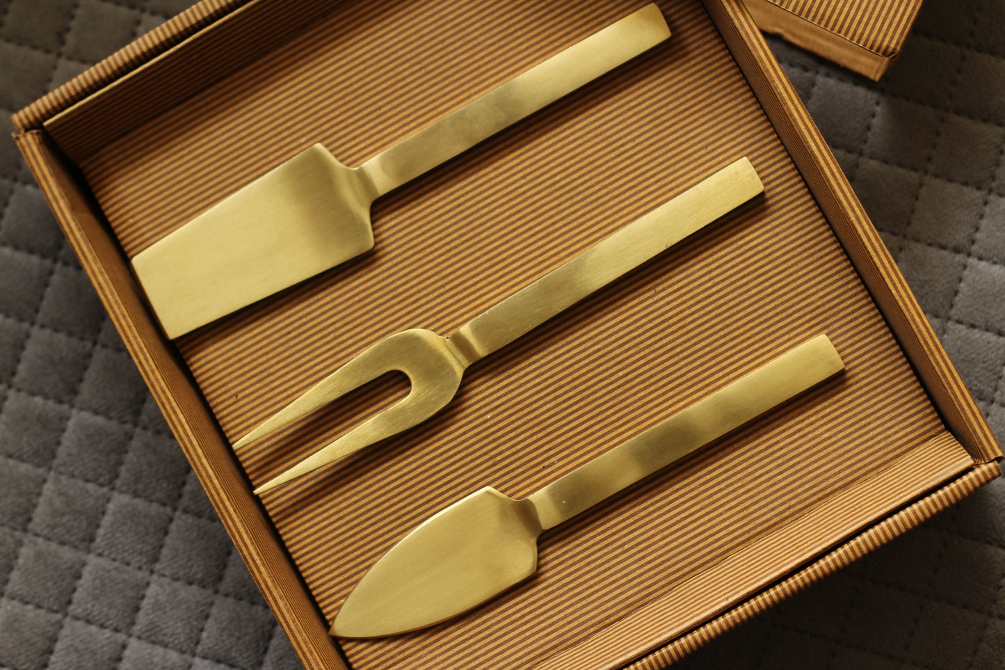 Top view of four elegant gold cheese knives arranged neatly on a cheese board.