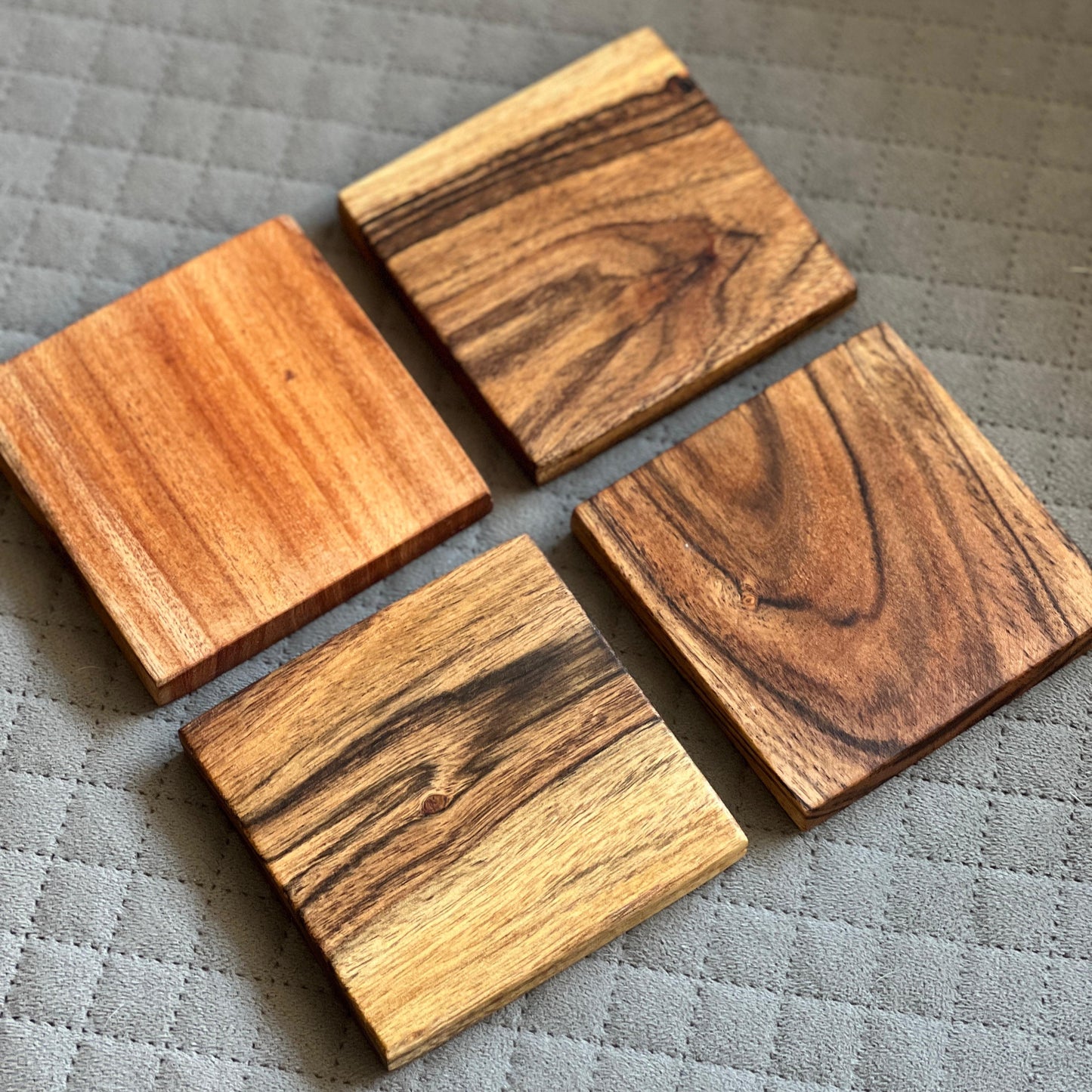Top-down view of four square acacia wood coasters stacked neatly on a wooden surface, showing natural grain texture.