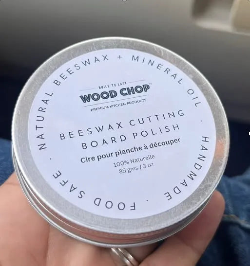 Beeswax container placed next to a wooden cutting board and spoon.