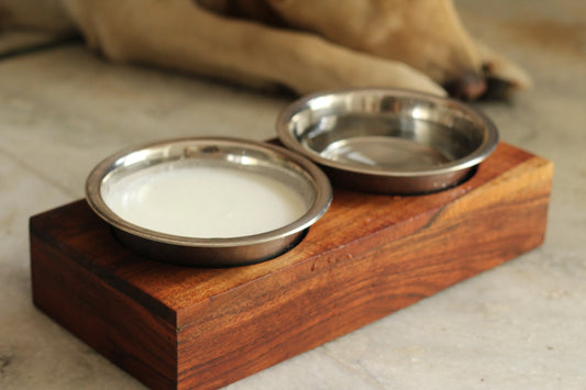 Top view of a wooden pet feeder with two stainless steel bowls filled with kibble and water.