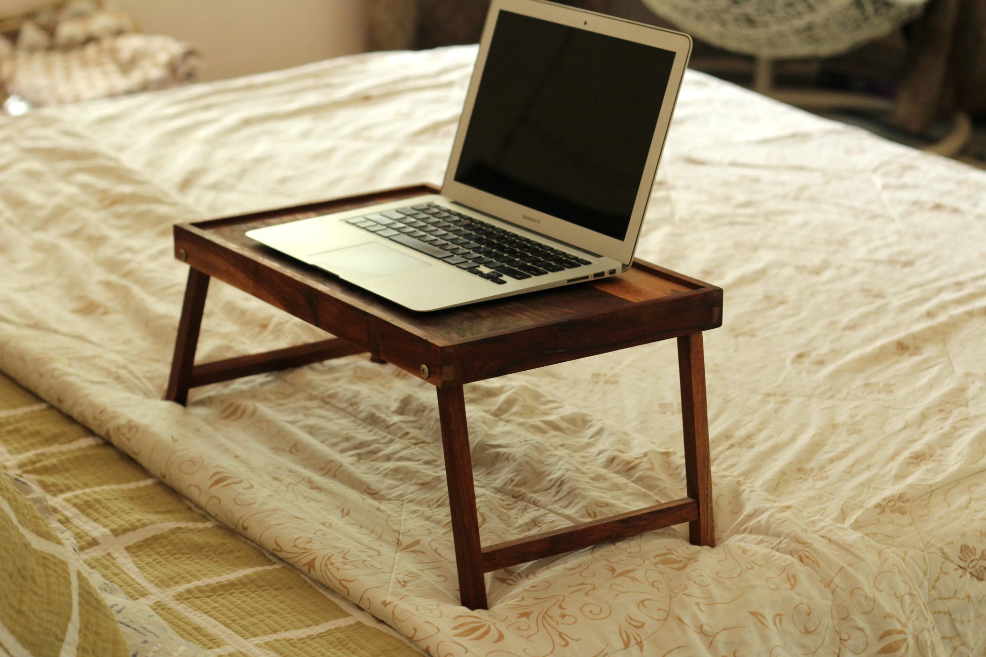  Foldable wooden laptable placed on a bed with a laptop and notebook on top.