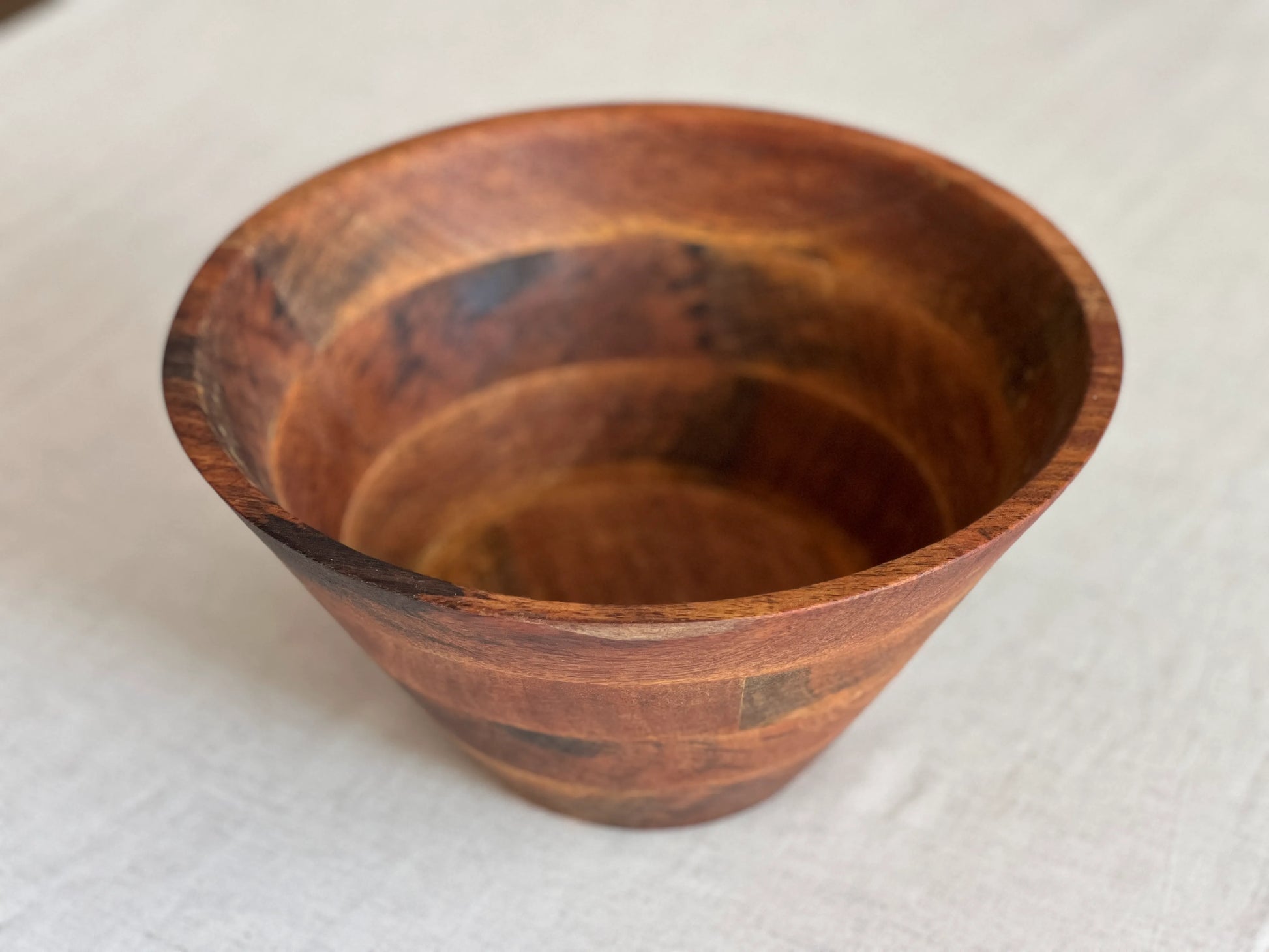 Empty wooden bowl placed on a dining table beside a salad serving set.