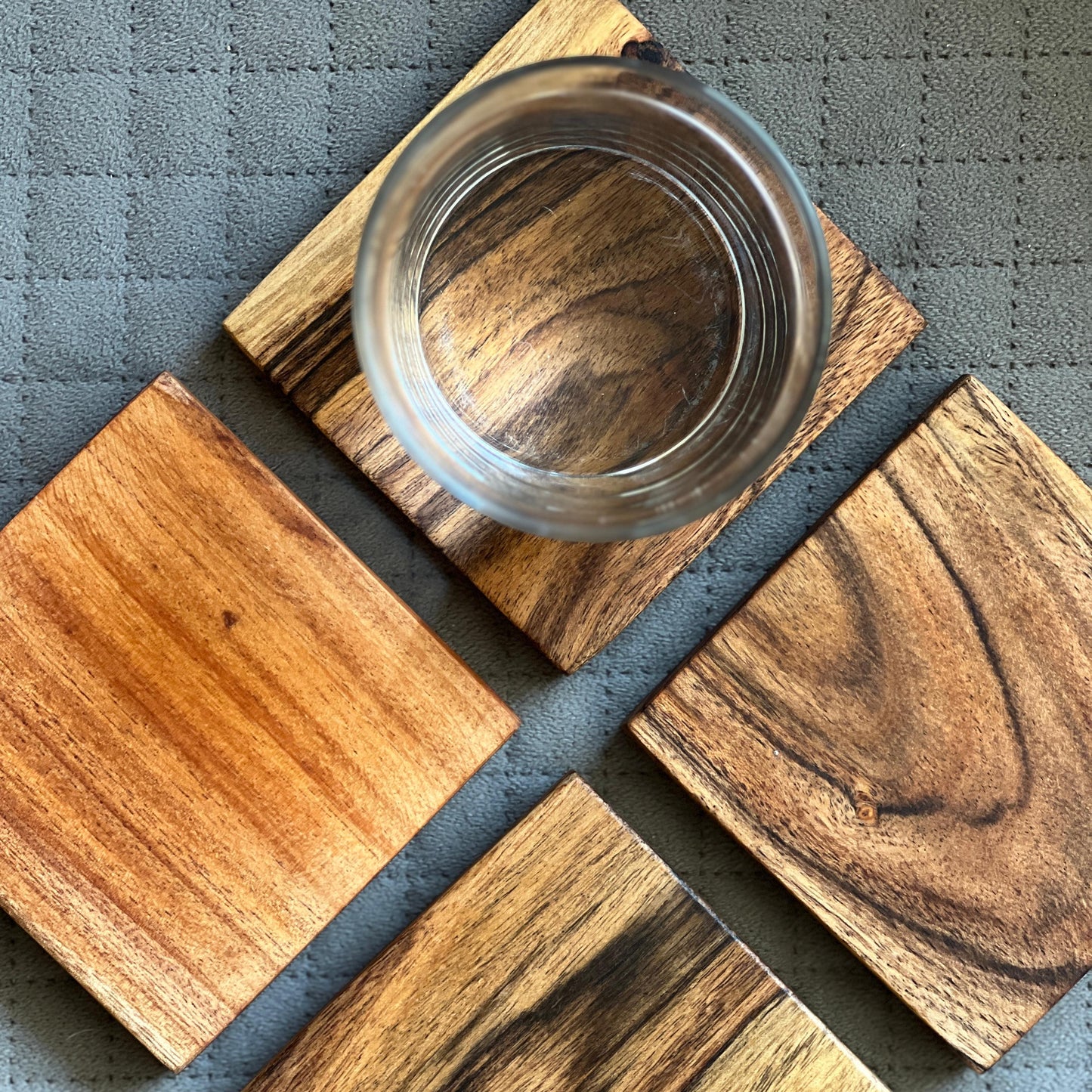 Set of 4 acacia wood coasters arranged side-by-side on a dining table, styled with cups and glasses.