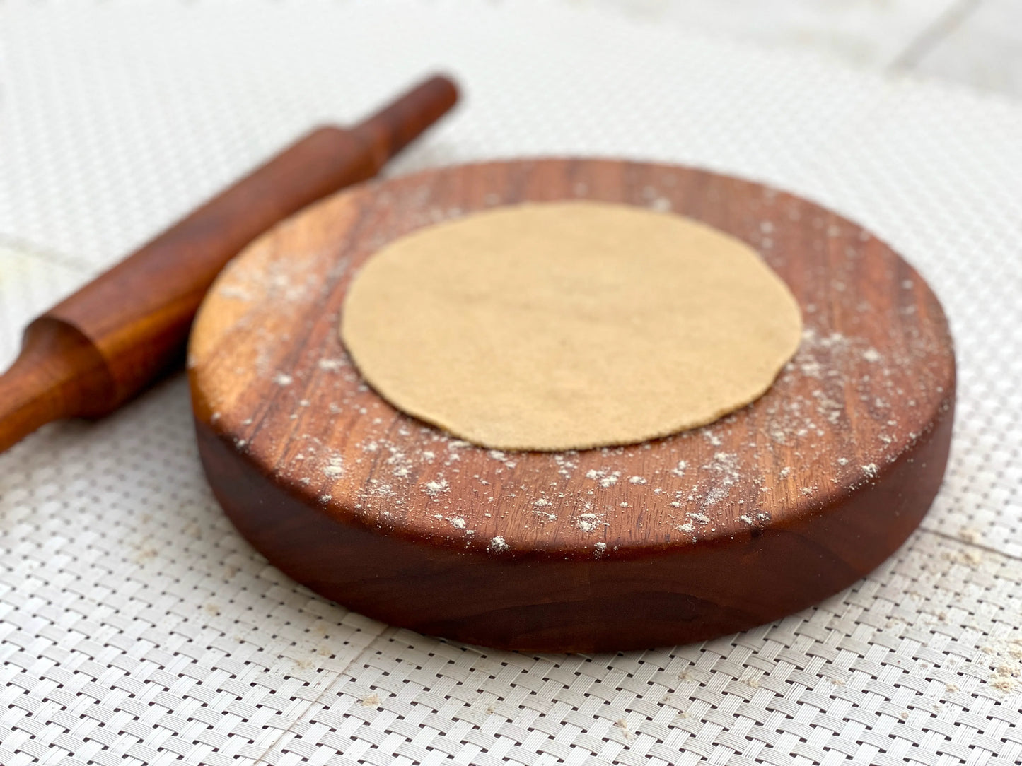 Rolling board used to prepare rotis, with dough balls and dry flour beside it.