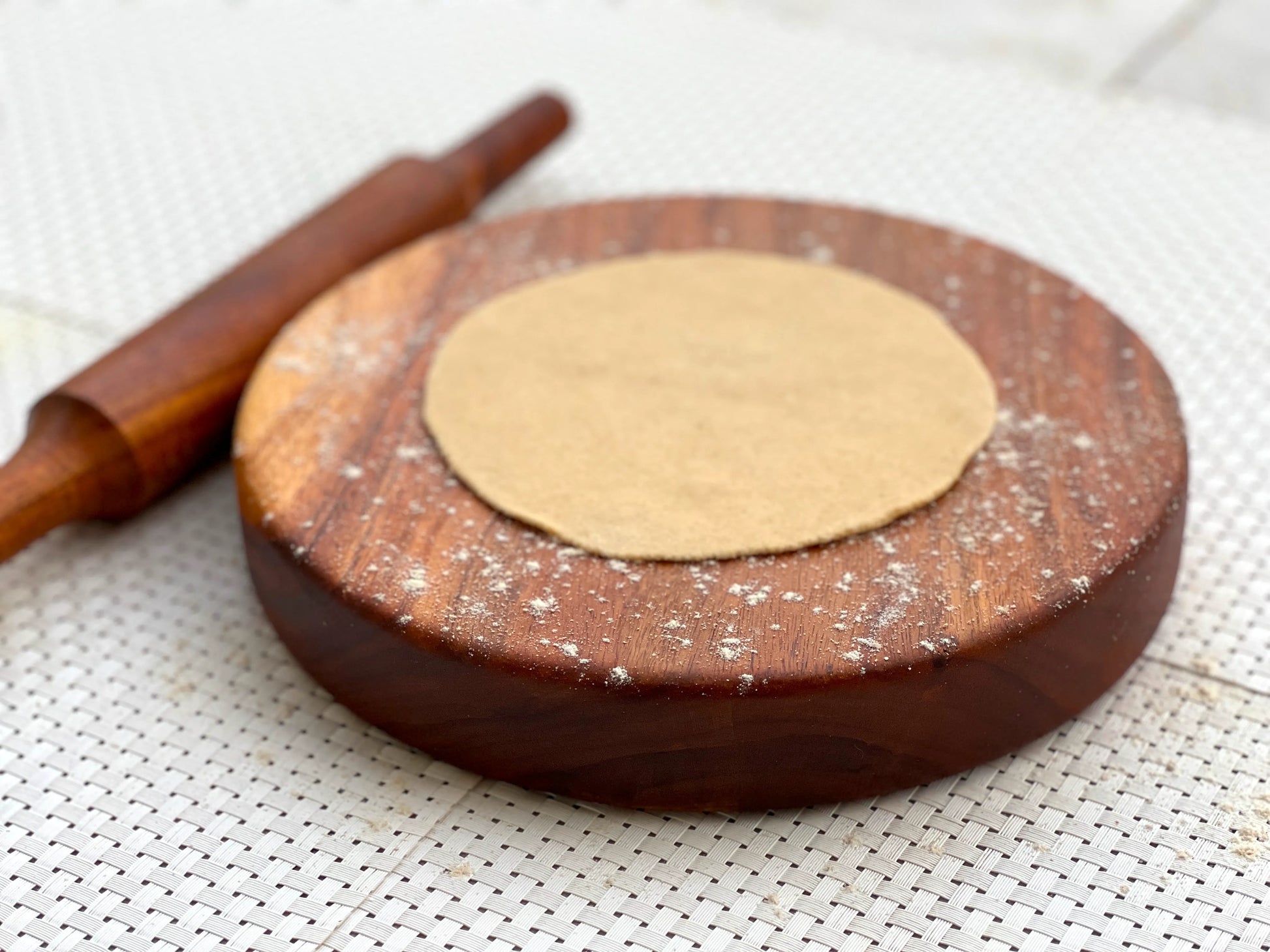 Rolling board used to prepare rotis, with dough balls and dry flour beside it.
