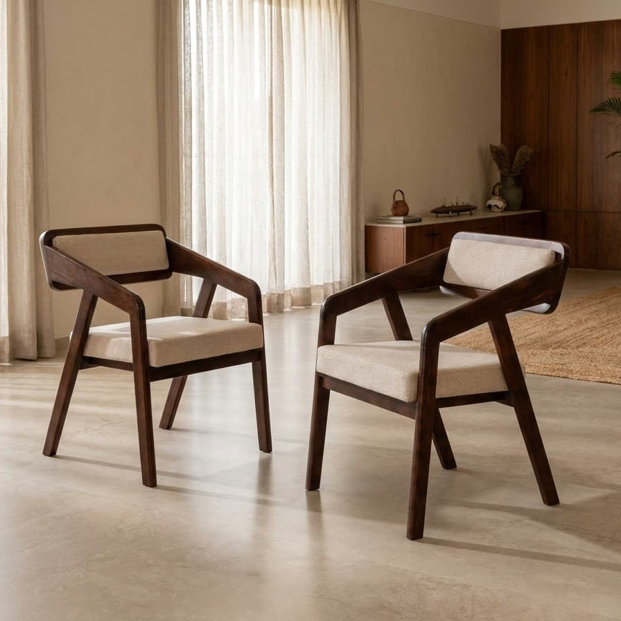 Two modern wooden dining armchairs with cream upholstered seats and backrests, shown in a bright, contemporary living room setting.