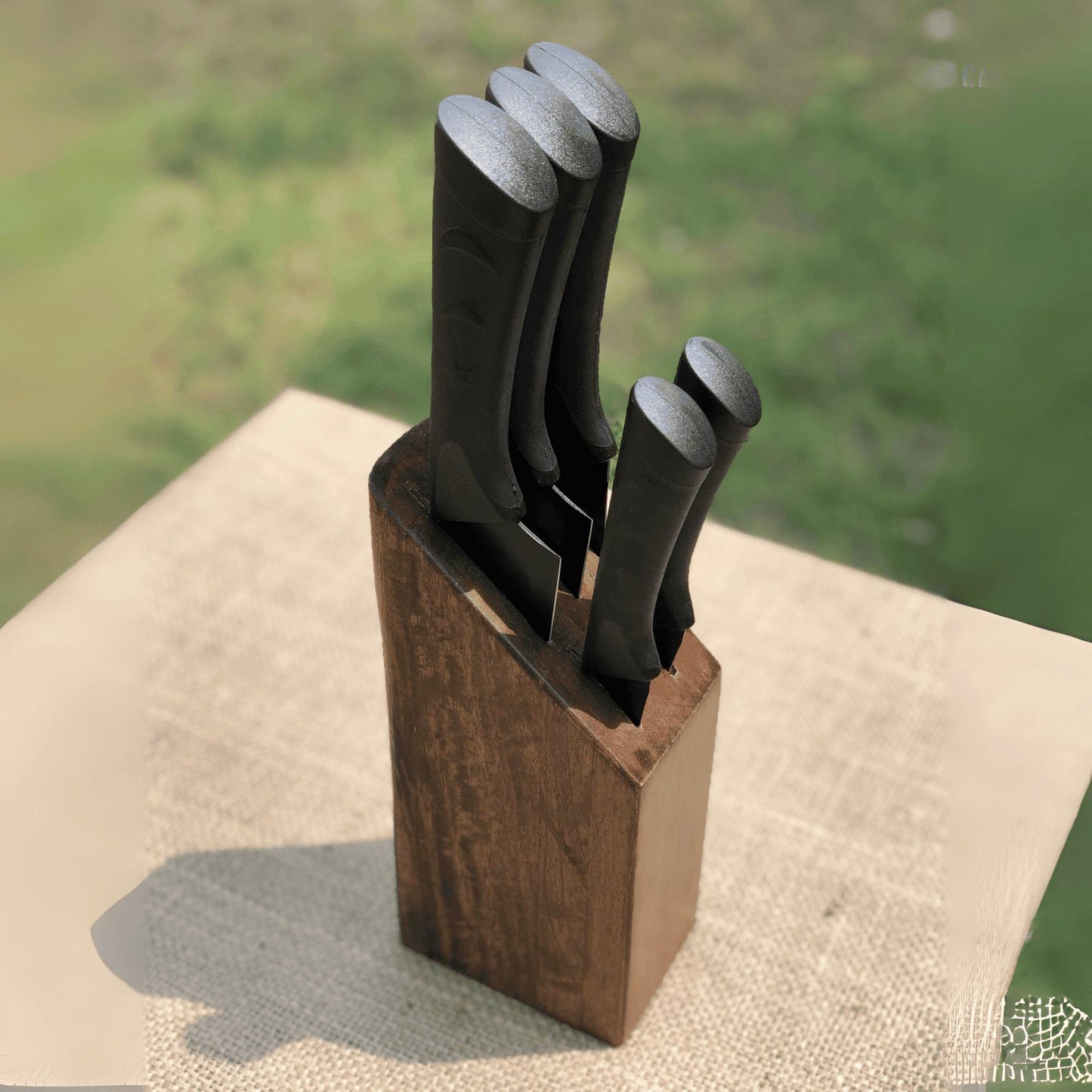 Set of knives in a wooden block on a textured surface with a blurred natural background