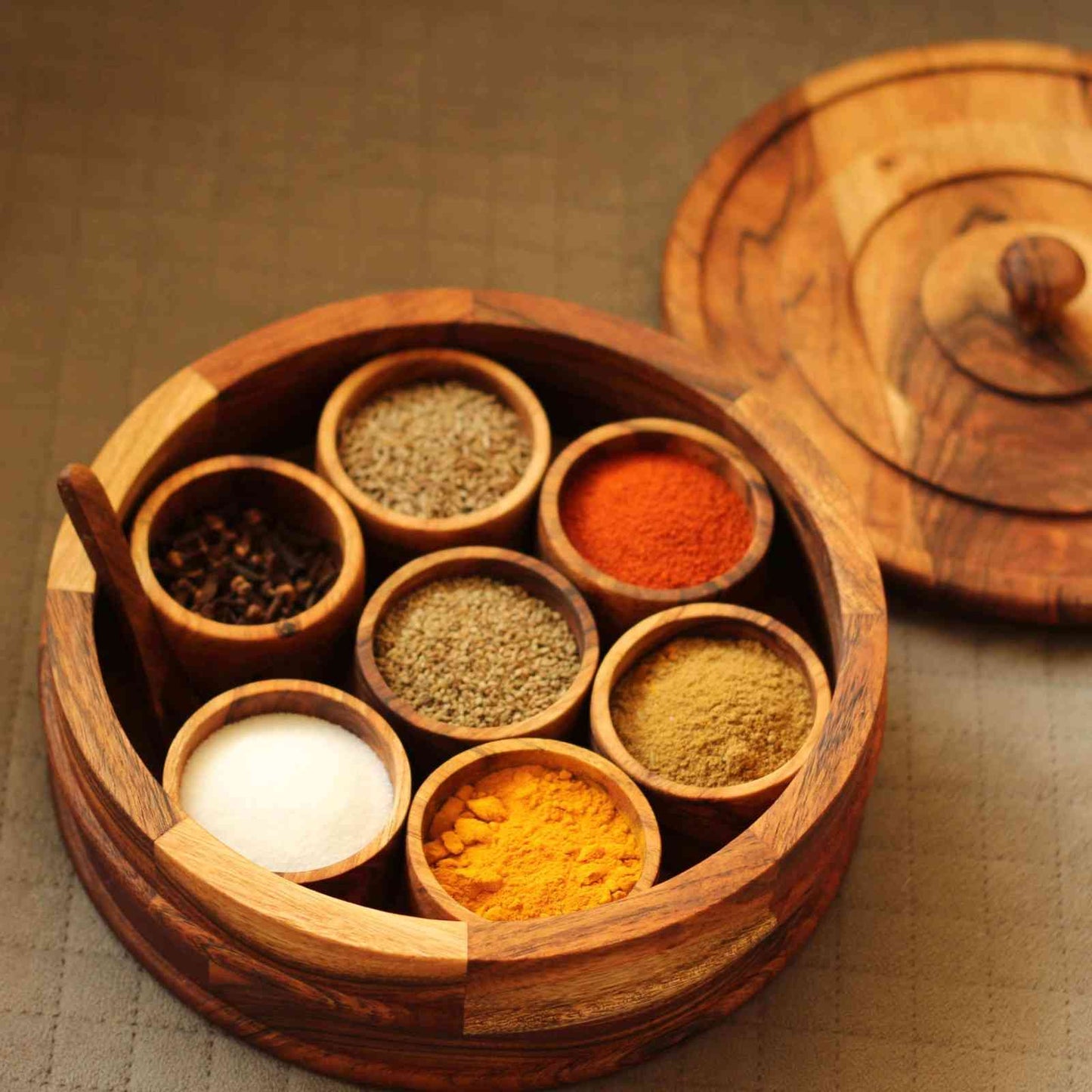 Wooden spice set with various spices in small compartments on a textured surface.