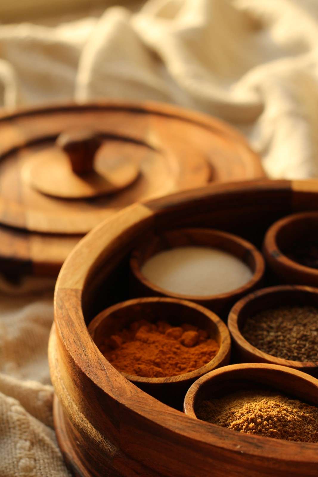 Wooden spice rack with various spices on a textured fabric background