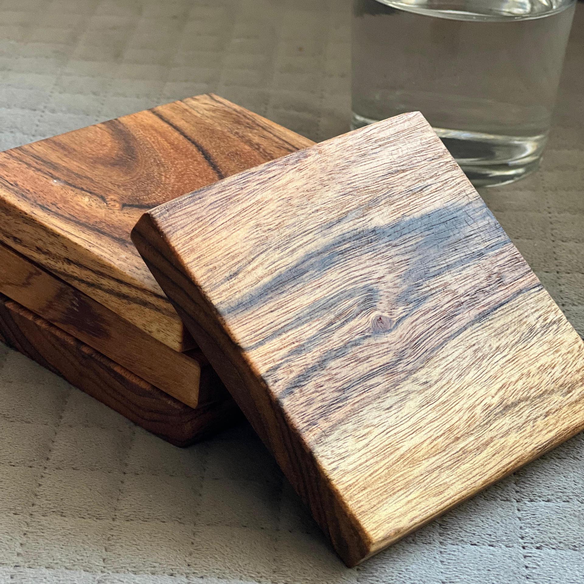 Wooden coasters on a textured surface with a glass of water in the background